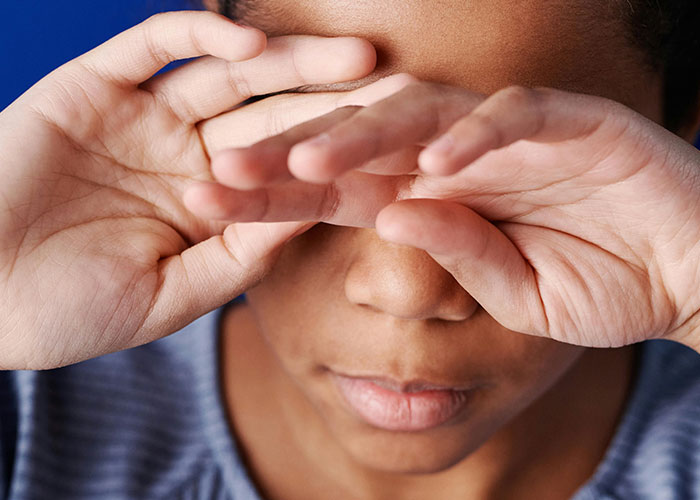 Child covering face with hands, possibly upset or tired, related to issues with teachers needing improvement.
