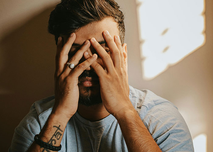 Man with tattoo and ring covering his face, showing heartbroken emotions related to cheating in a relationship.
