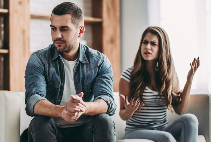 Man and woman on a sofa, woman expressing frustration, man looking away.