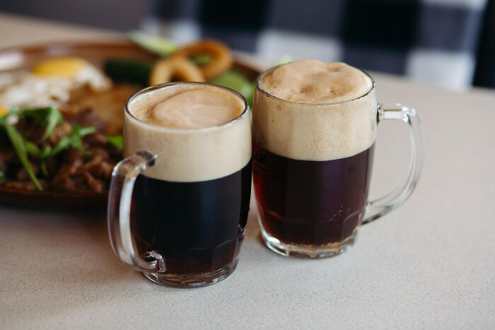 Two mugs of dark beer with foam on a table, highlighting quirky American dining habits.