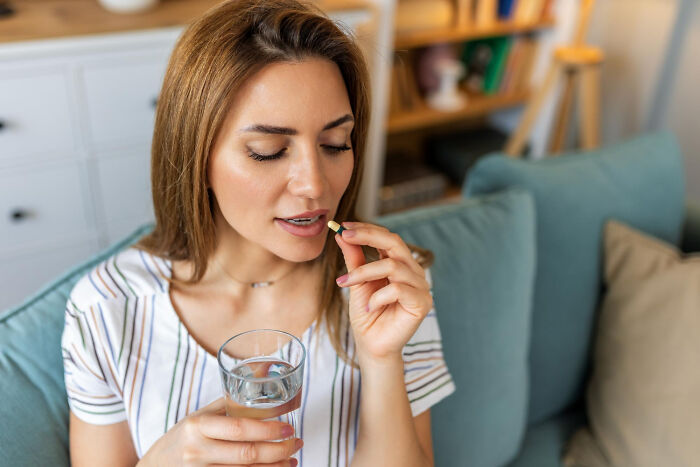 Woman sitting on a couch, about to take a pill with a glass of water, illustrating scientific advancements.