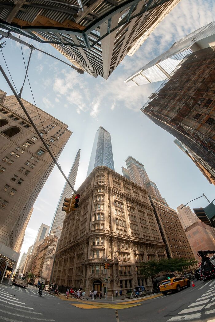 Fisheye view of towering skyscrapers and lesser-known architectural wonders in a bustling city intersection.