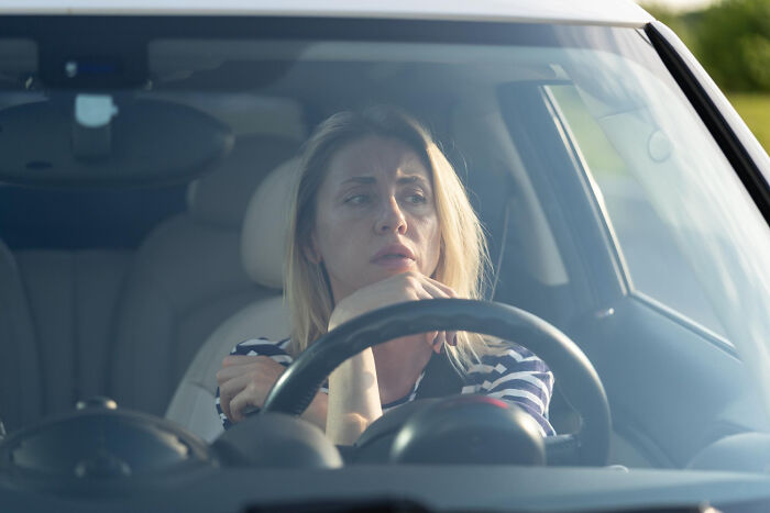 A woman in a car looking thoughtful, symbolizing parental regrets and therapy.