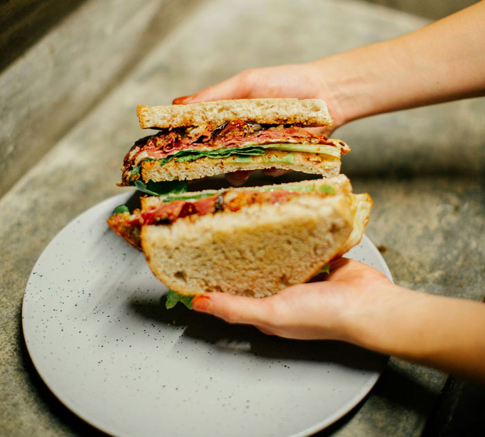 Hands holding a large sandwich over a plate, symbolizing being close to parents' meals and traditions.