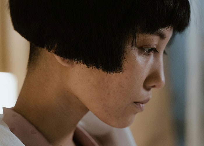 Young woman with short black hair looking down sorrowfully, reflecting on heartbreak and cheating in a relationship.
