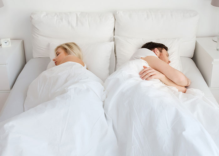 A couple lying back to back in bed, illustrating a moment of disconnect in marriage relationships and communication.