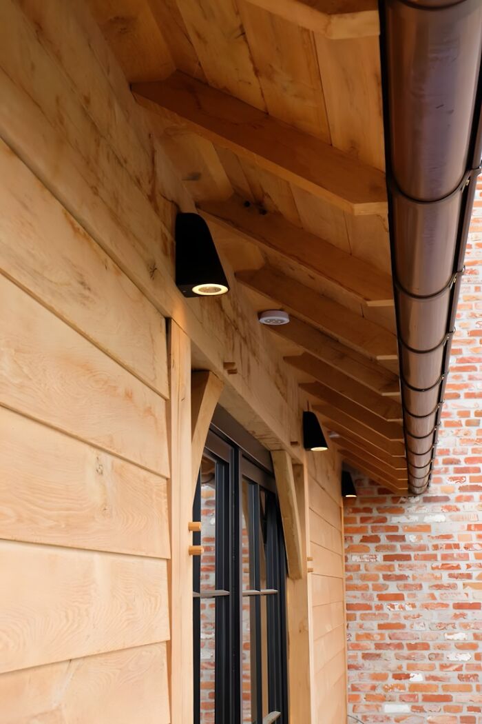 Close-up of wooden siding and roof beams with black outdoor lights showcasing woodworking ideas on home exterior.