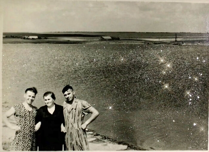 Three people standing by a lake under a cloudy sky, evoking themes of love without boundaries.