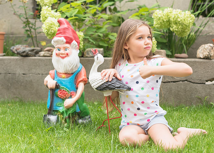 Child in garden with gnome statue and bird decor, illustrating bizarre HOA decor ideas.