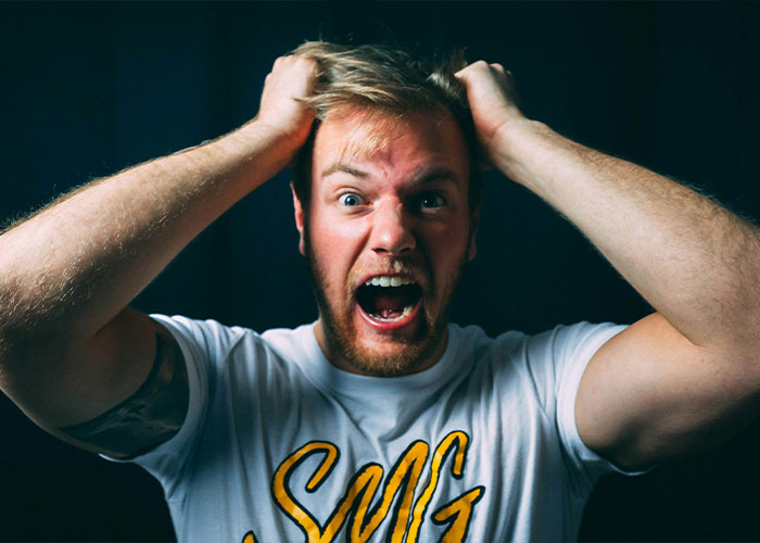 Man in a white shirt looking frustrated with hands on head, highlighting Duke Dennis hug theme.