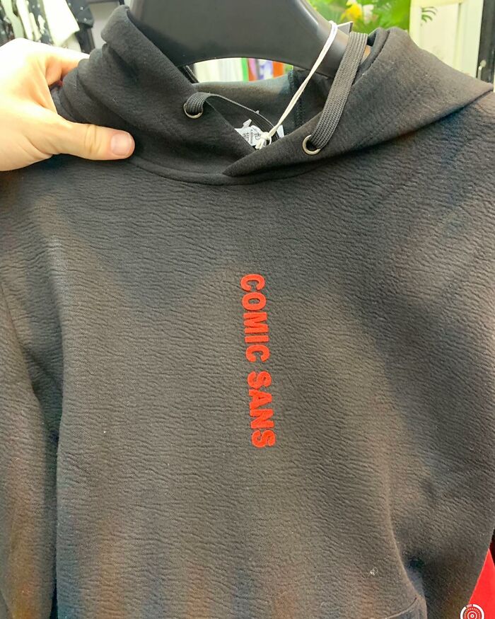 Black hoodie with "COMIC SANS" in red text, showcasing a humorous translation mishap on apparel.