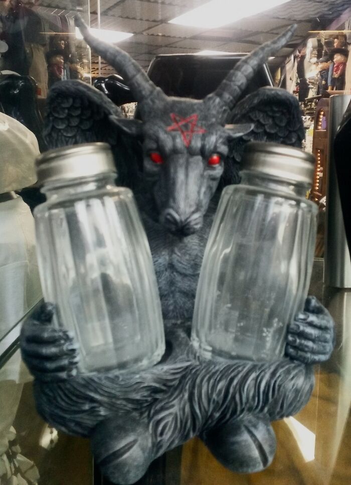 Demonic goat statue with red eyes in a secondhand shop, holding glass jars, symbolizing bizarre treasures.