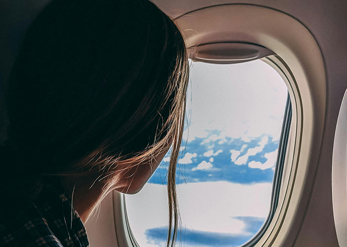 Person gazing out airplane window, clouds visible, illustrating surprising plane experience.