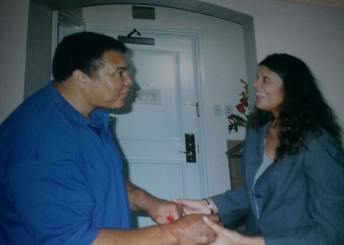 Celebrity in a blue shirt warmly greeting a smiling woman in a grey blazer.