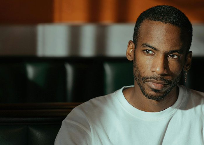 Man in a white shirt sitting thoughtfully in a dimly lit room, reflecting on heartbroken people revealing cheating signs.
