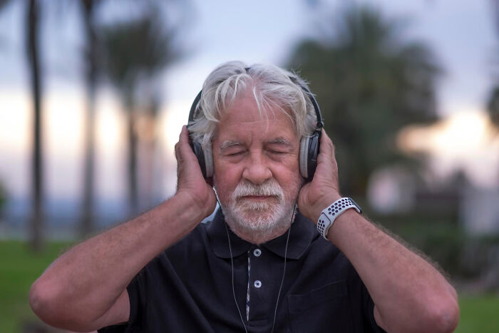 Elderly man enjoying music with headphones, outdoors, representing aging realities.