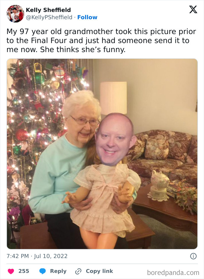Elderly woman humorously posing with a doll featuring a human face by a Christmas tree.