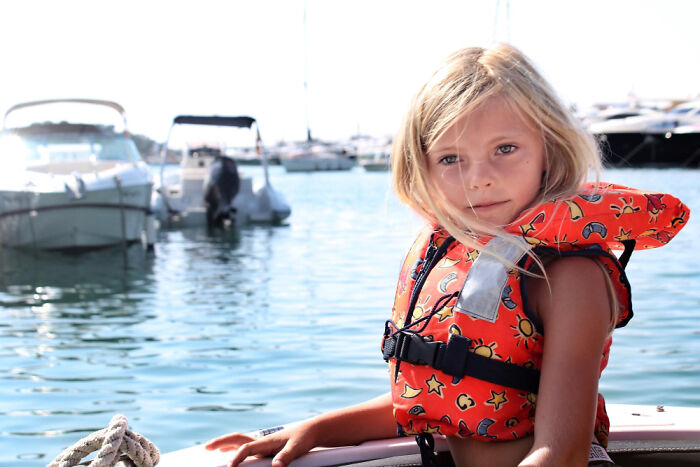 Young girl in a bright life jacket on a boat, highlighting intuition and safety near a marina.
