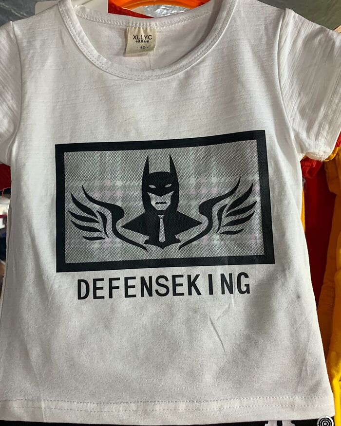 A white T-shirt with a quirky graphic of a bat-like figure labeled "DEFENSEKING," exemplifying funny translation errors.