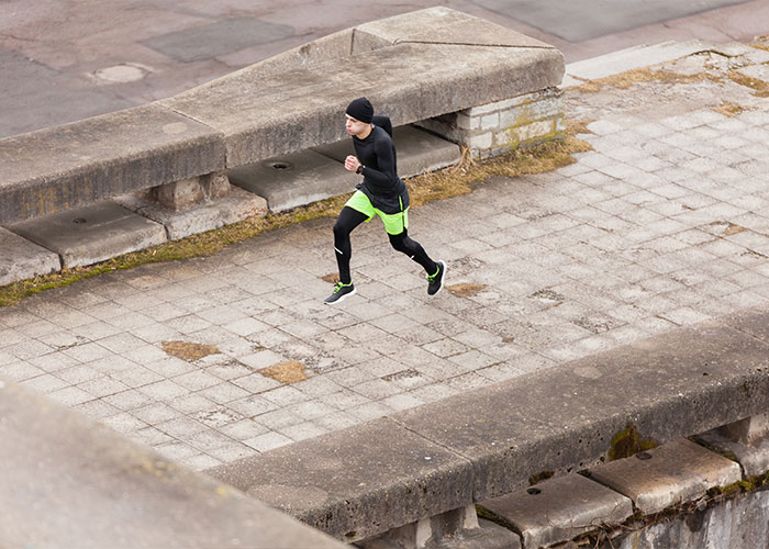 Person jogging on urban pavement in black and neon athletic gear, showcasing unrealistic movie-like scenario.
