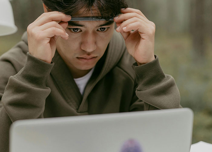 Young man in a green sweatshirt looking worried while using a laptop, reflecting heartbroken people revealing cheating signs.