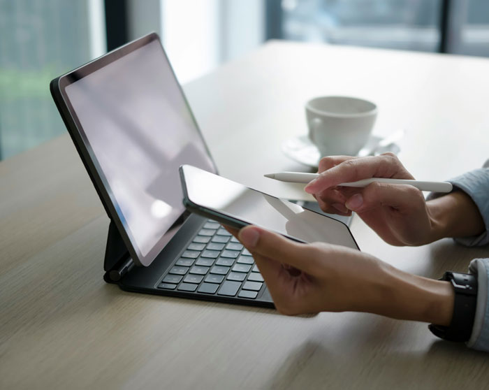 Person using tablet with keyboard and smartphone, holding stylus, working on digital SEO deliverables at a desk.
