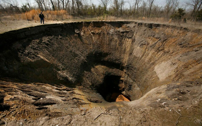 Deep sinkhole in a barren area with a person standing at the edge, illustrating a scary phenomenon.