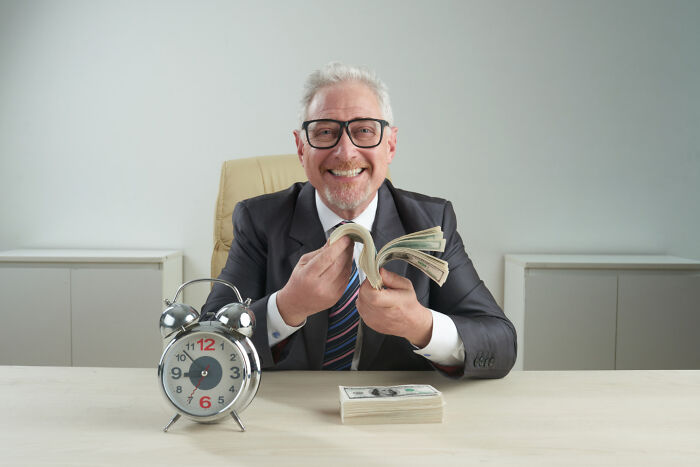A man smiling in a suit with an alarm clock and money on a desk, illustrating a humorous take on things that can keep us up at night.