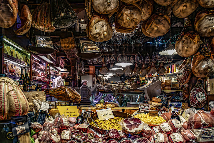 A bustling Italian market with cured meats, cheese, and pasta, illustrating World Food Photography Awards 2025 shortlist.