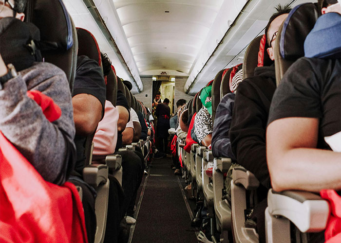 Passengers seated on a plane, some sleeping, in a crowded cabin setting.