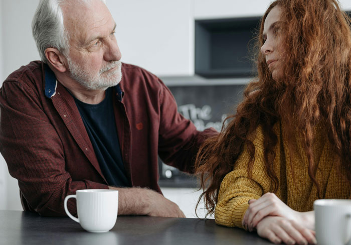 An older man and a younger woman sharing a meaningful conversation at a table, conveying emotions of love and surprise.