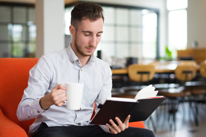 Man in a white shirt holding a mug and reading a notebook, illustrating ridiculous questions in job interviews concept.