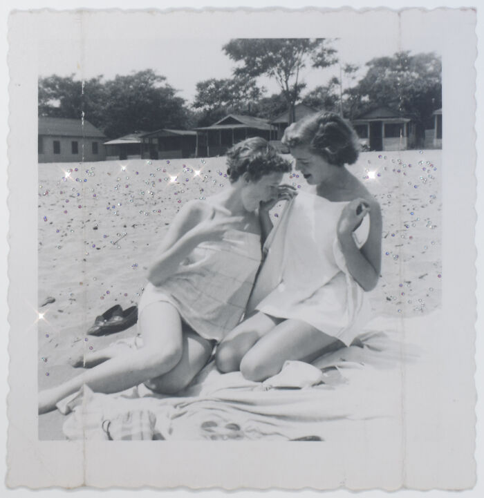 Two women sitting closely on a towel at the beach, sharing a moment of laughter—a love without boundaries.