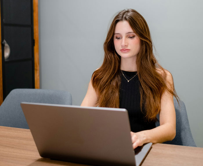 Young woman at a desk using a laptop, concerned about a canceled doctor's appointment.