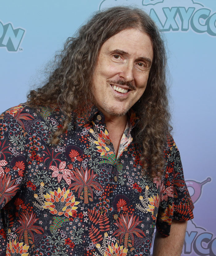 Smiling man in a floral shirt at convention, showcasing beloved star charm.