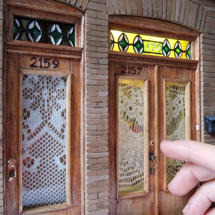 Fingers pointing at intricate miniature doors with lace panels, showcasing Tamar Cohen's mesmerizing tiny worlds.