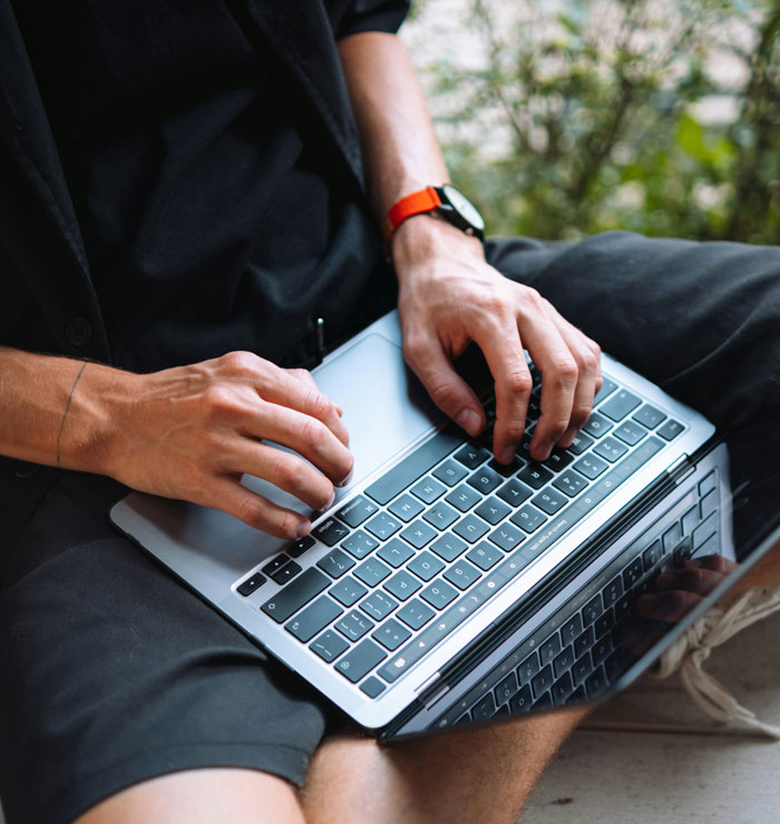 Person typing on a laptop, utilizing internet hacks for easier online life, wearing a black outfit and red wristwatch.