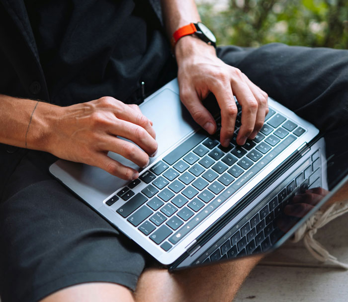 Person typing on a laptop, focused on submitting SEO deliverables using unconventional and unethical work hacks.