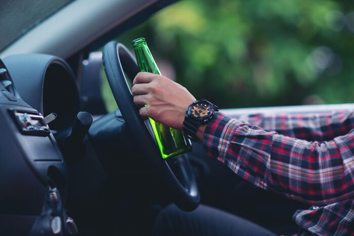 Person in plaid shirt holding a bottle while gripping a car steering wheel, highlighting parental favorites regret.