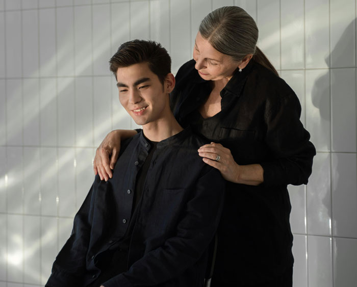 Young man with an older woman, both smiling closely, in a tiled room, illustrating a close parent relationship.
