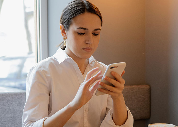 Young woman in a white shirt looking at her phone, reflecting on heartbreak and cheating in relationships.