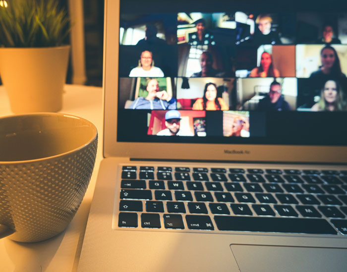 Laptop screen showing a virtual meeting with multiple participants and a cup of coffee nearby, illustrating online work hacks.