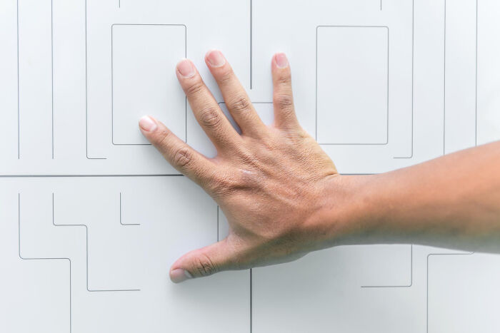 A hand placed on a geometric pattern, evoking bizarre and slightly creepy house rules.