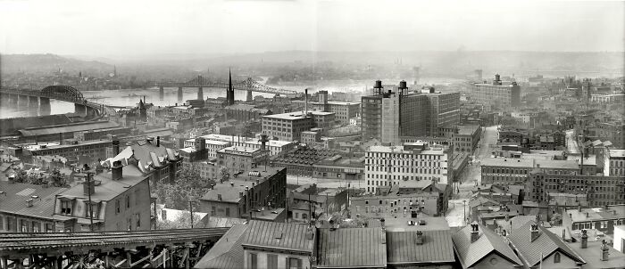 Historic black and white cityscape showing life in America from 100 years ago with industrial buildings and bridges.