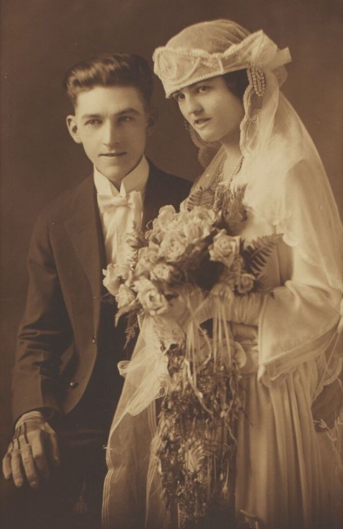 Vintage wedding couple, the groom in a tuxedo and the bride in a lace veil, holding a bouquet of roses.
