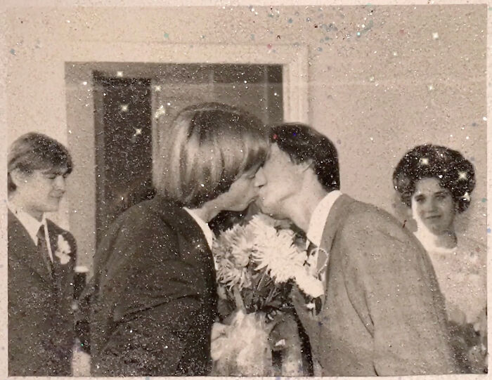 Two people share a kiss, celebrating a love without boundaries, holding flowers in a vintage photo setting.