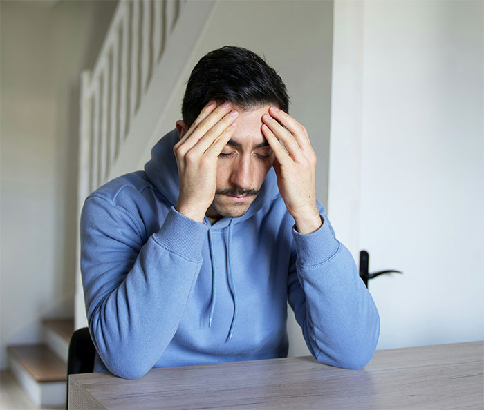 Man in blue hoodie with head in hands, feeling stressed about babysitting situation.