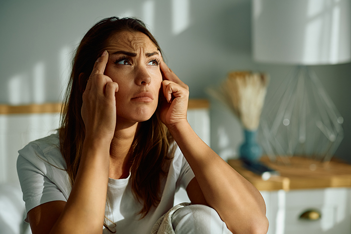 Woman deep in thought, expressing concern, in a sunlit room regarding MIL jokes about birth control.