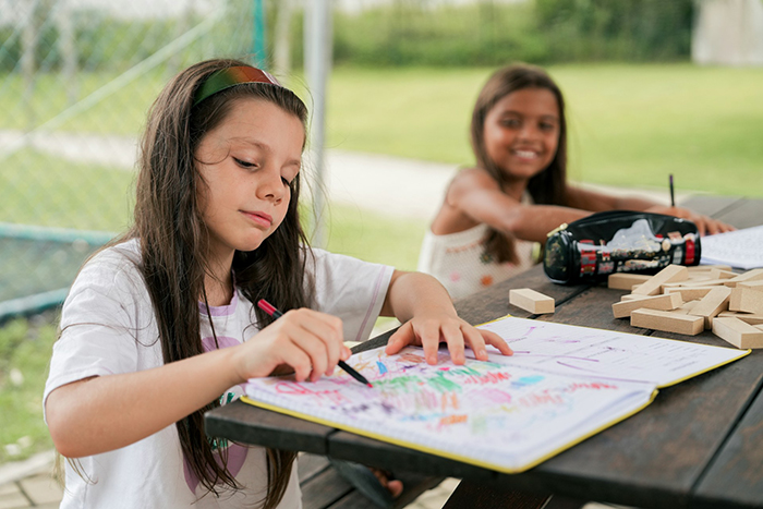 Two girls coloring at a picnic table, showcasing play date activities in an outdoor setting.