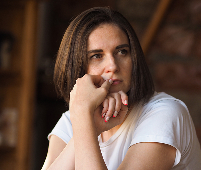Woman in deep thought, resting her head on her hand, wearing a white shirt indoors.